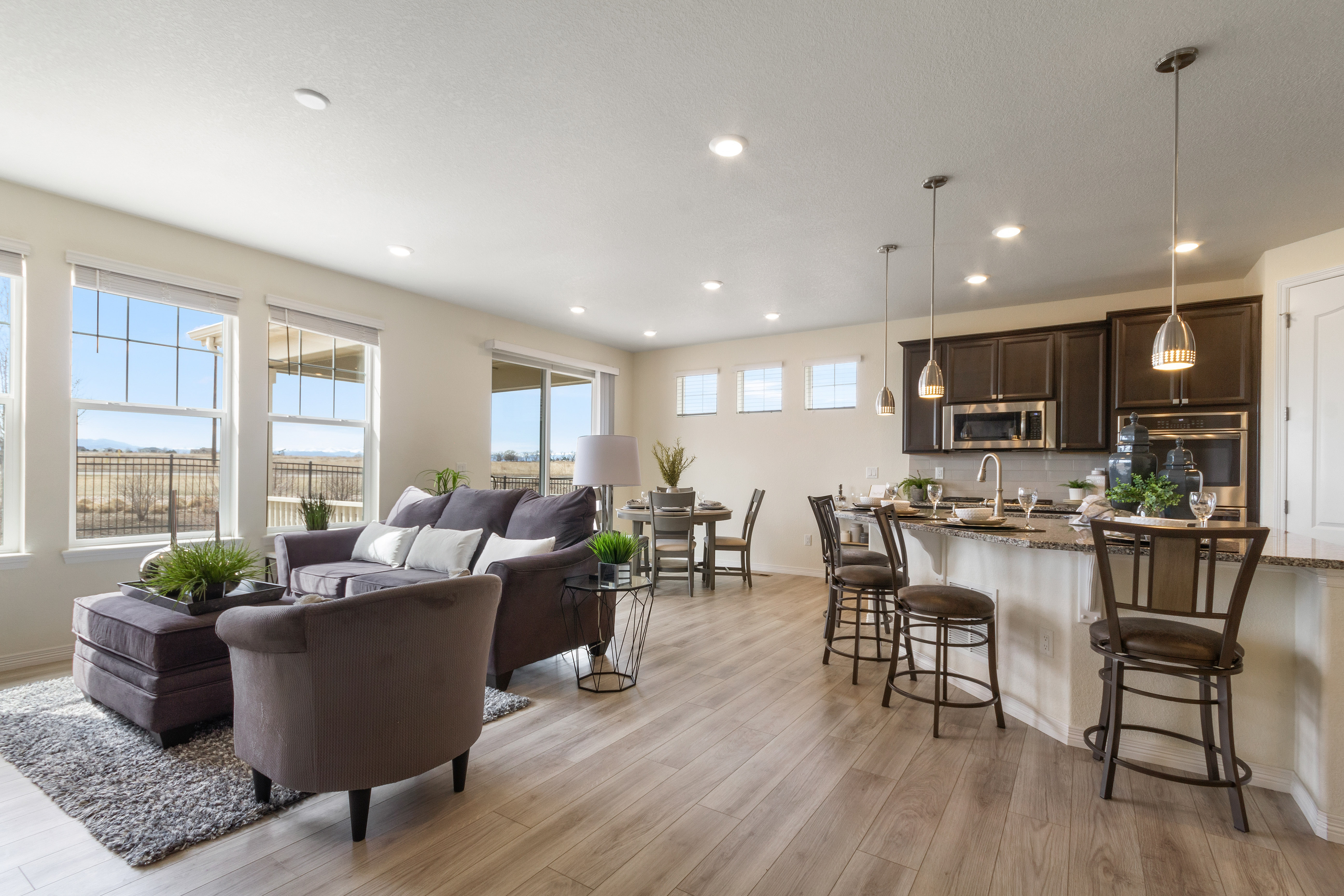 Open living room and kitchen with large windows, beige walls, wood flooring, and modern furnishings.