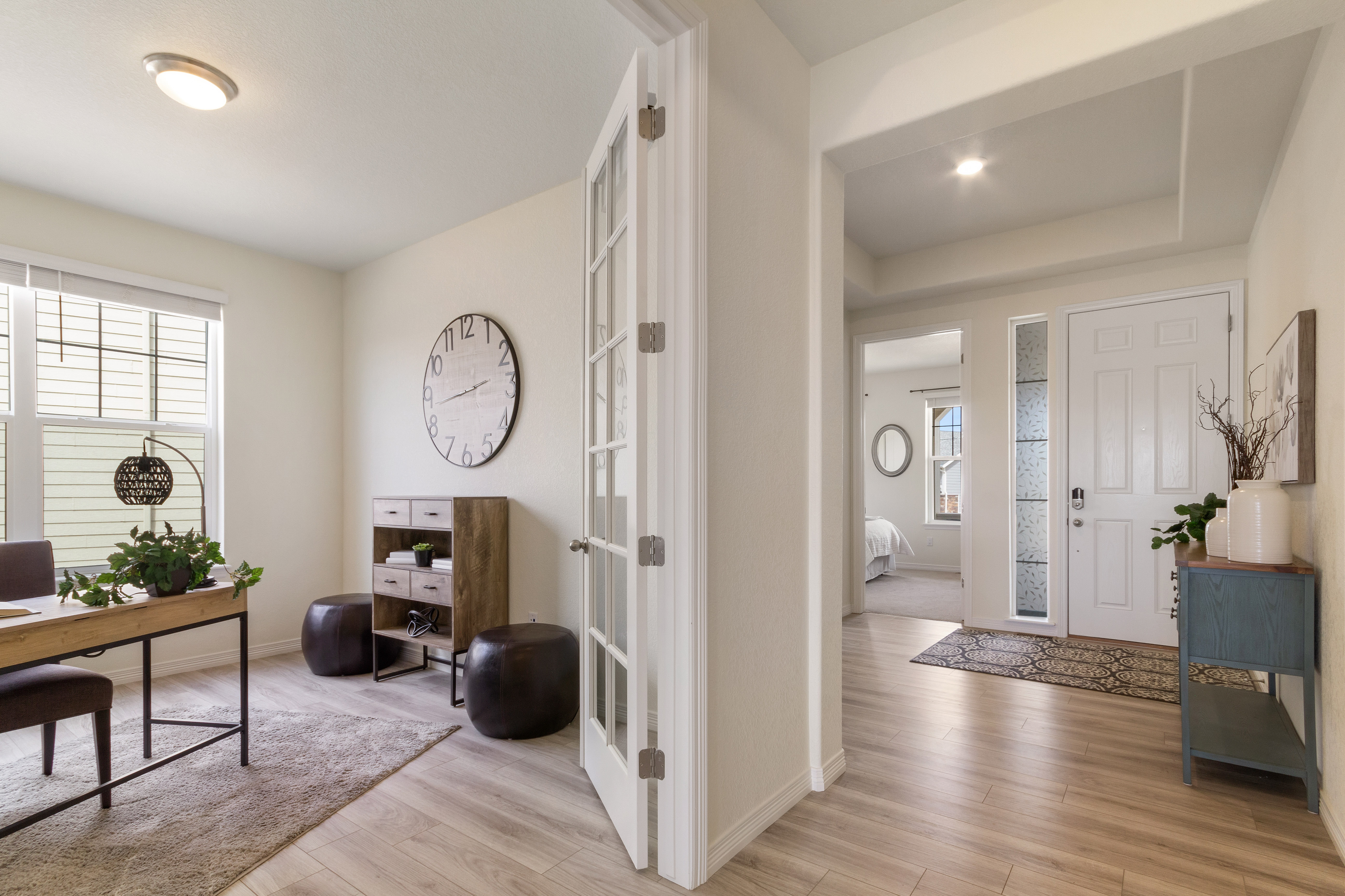 Bright modern home entry with wooden floor, blue table, and adjacent office space with desk and clock.
