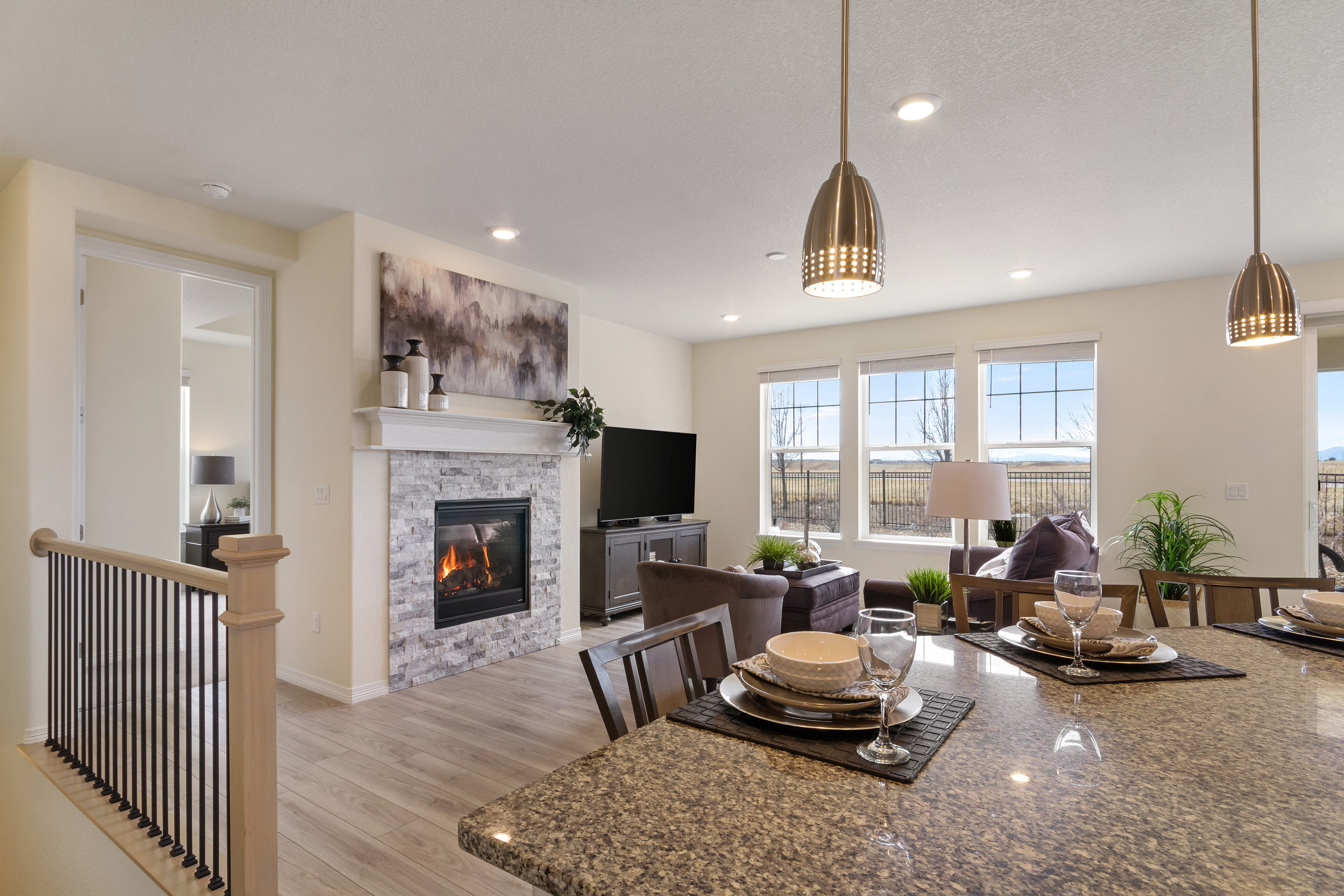 Bright living room with stone fireplace, TV, seating, and dining table set under pendant lights.