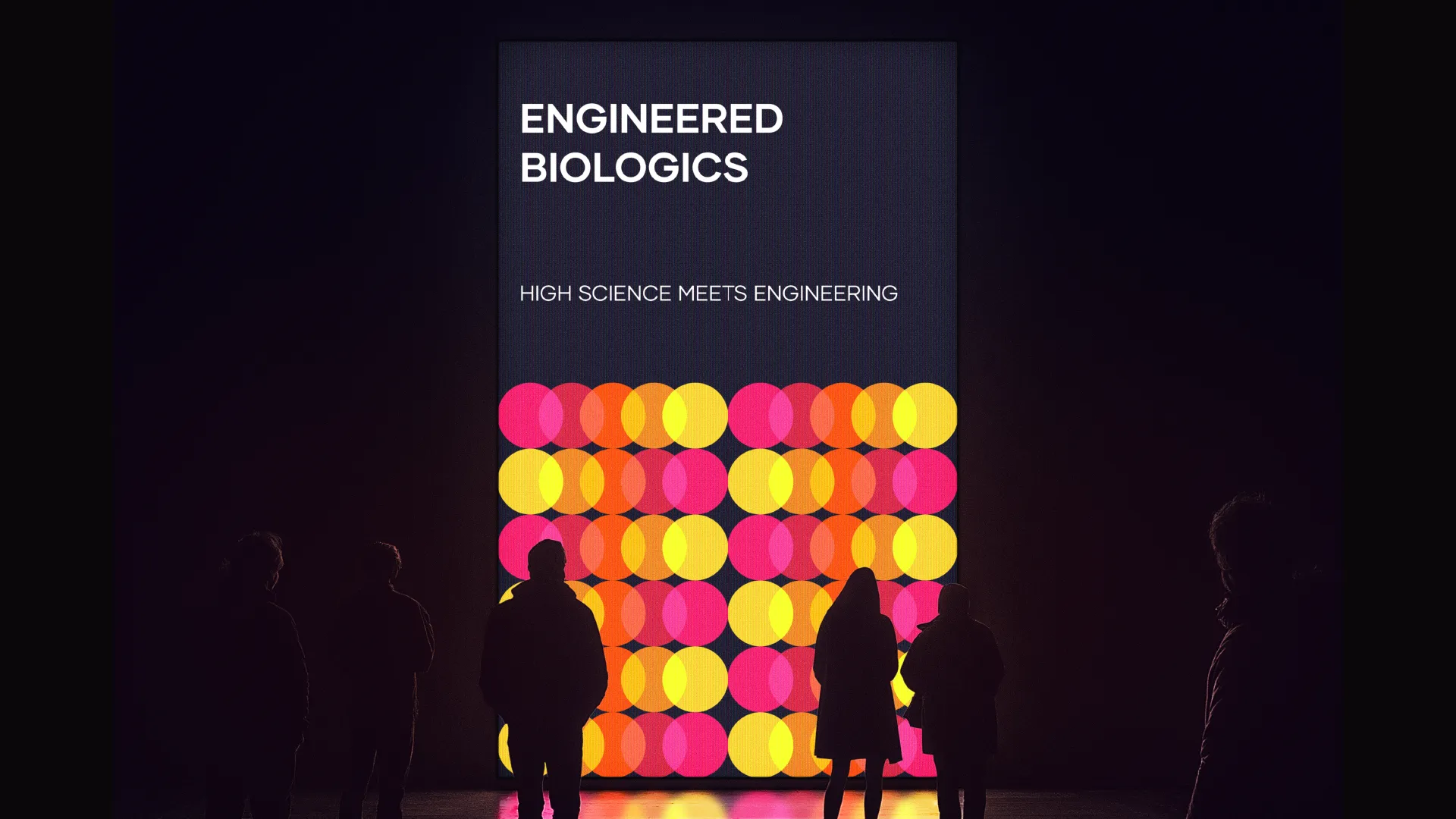 Silhouettes of five people standing in front of a large illuminated screen displaying colorful overlapping circles and the text 'Engineered Biologics High Science Meets Engineering'.