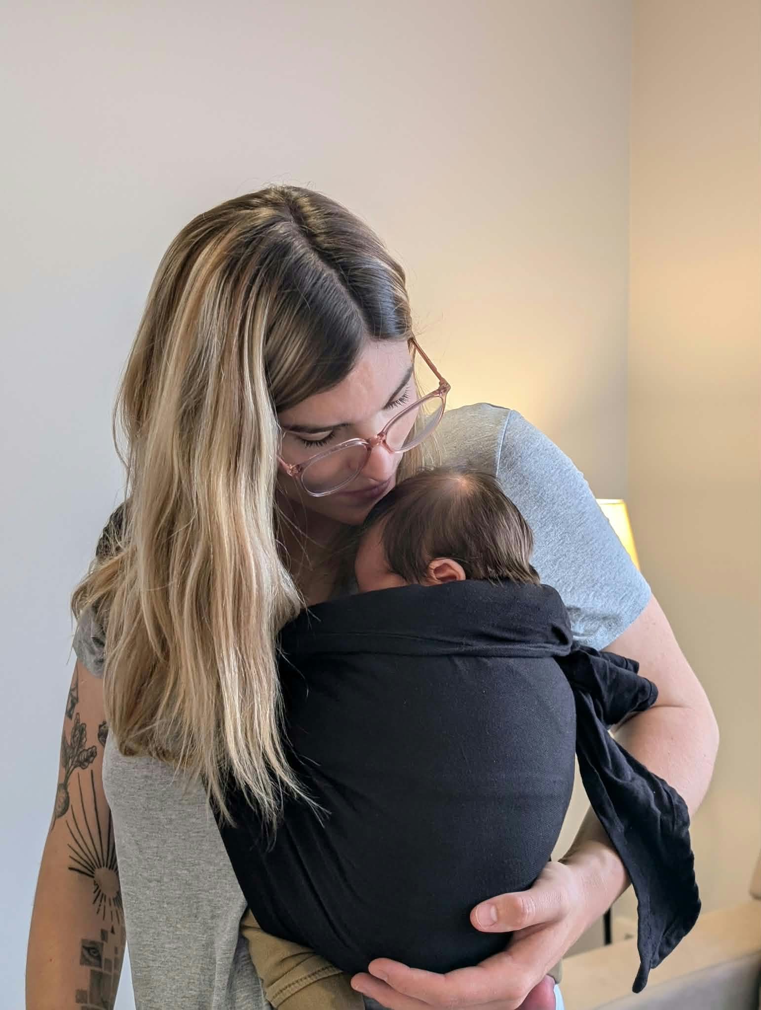 Parent qui donne un bisou sur la tête de son nouveau-né porté en écharpe