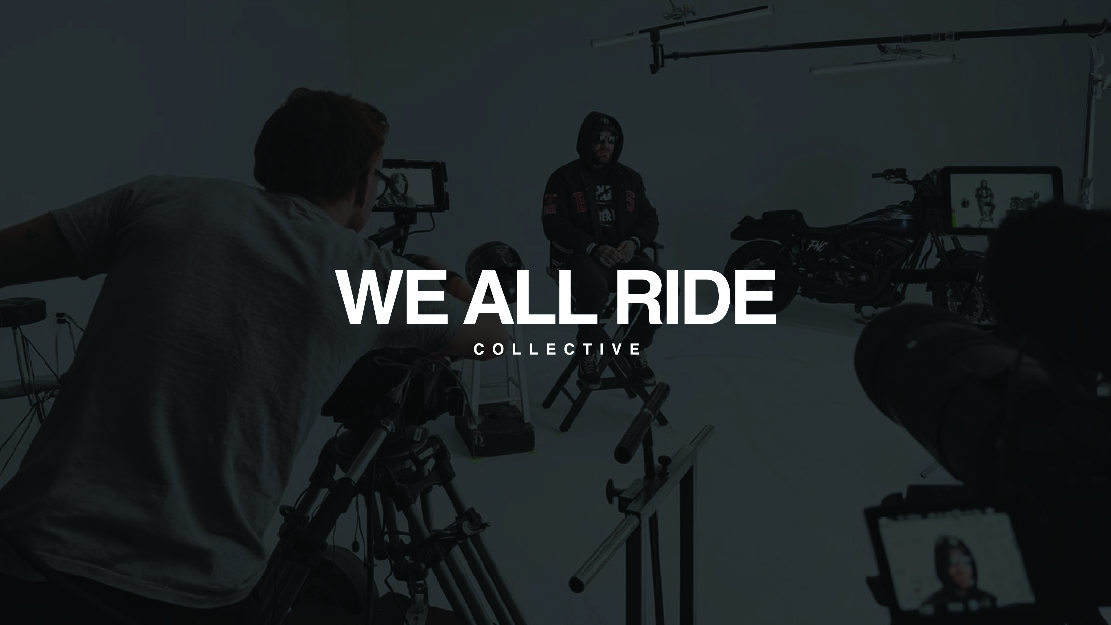 Image in a studio with cameras and camera man in the foreground, a man in a chair ready for an interview in the middle ground and lights and a motor cycle in the background. We All Ride Collective logo is placed on top of the image