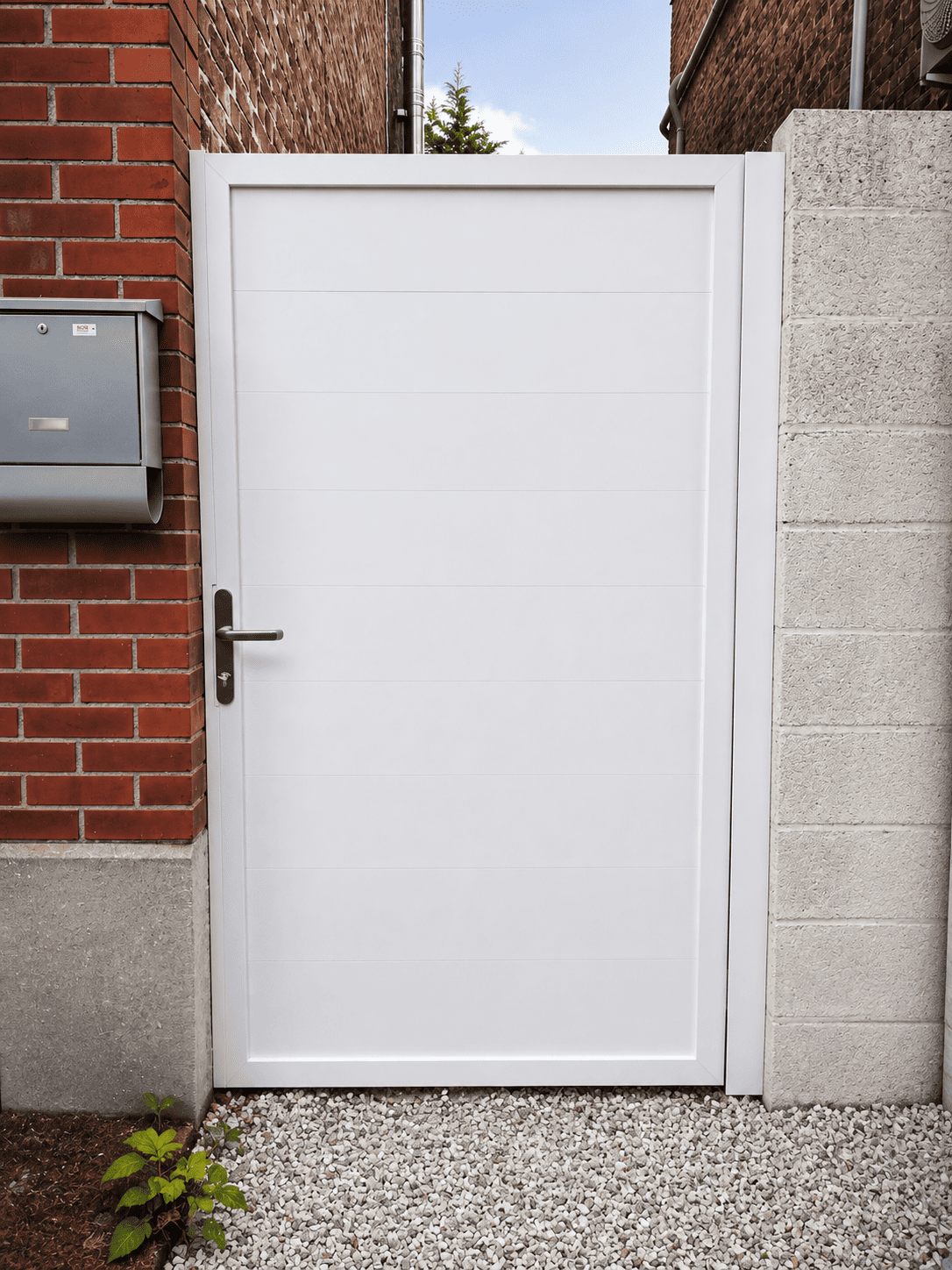 Portillon blanc moderne avec poignée métallique entre mur en briques rouges et mur en béton gris.