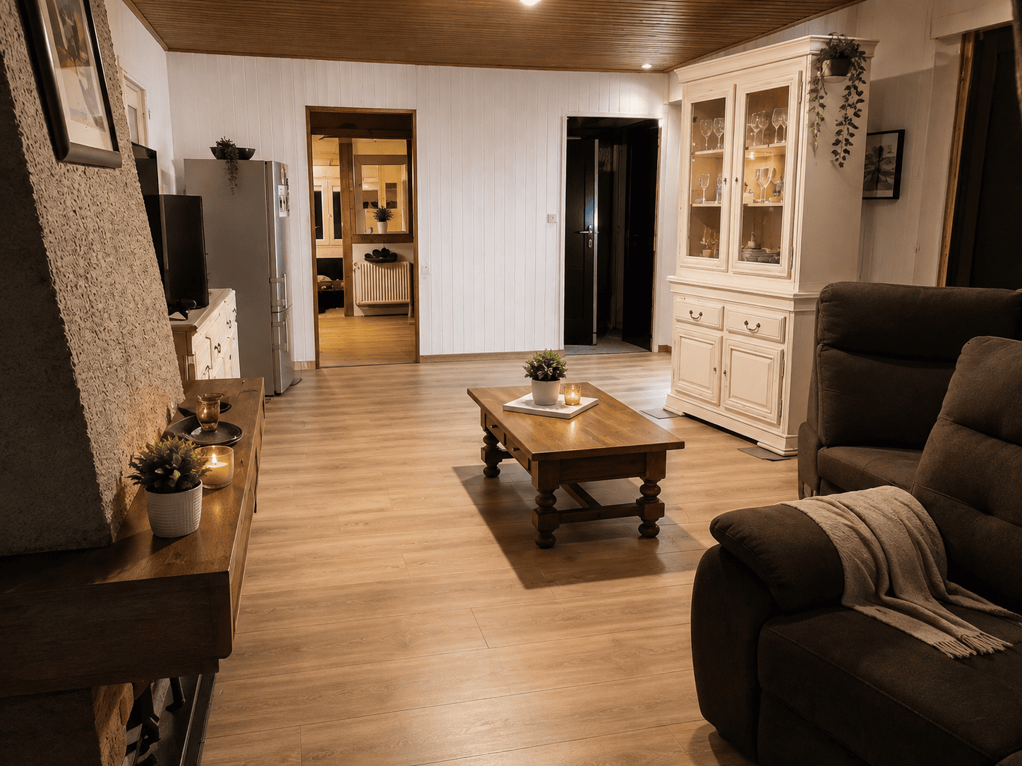 Salon avec parquet en bois clair, table basse, canapé marron et buffet blanc éclairé.