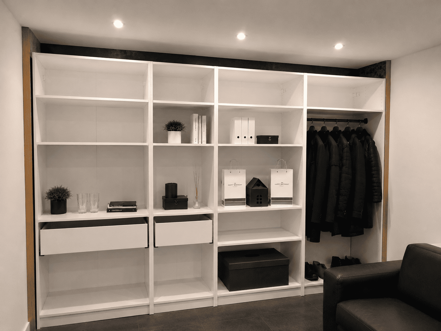 Dressing blanc avec étagères, tiroirs, vestes noires suspendues et chaussures en bas.
