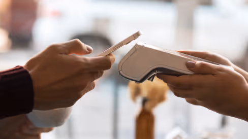 Person holding a smartphone near a contactless payment terminal held by another person.
