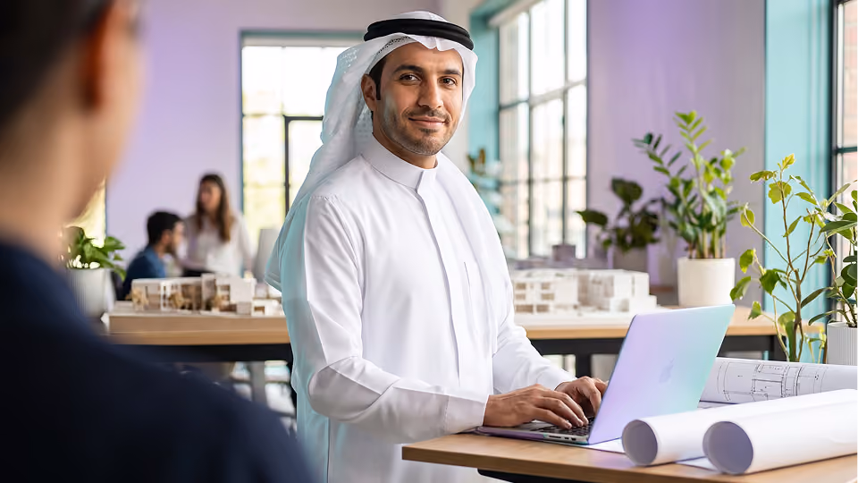 Smiling man in checkered keffiyeh and white thobe holding card, paying at a terminal.