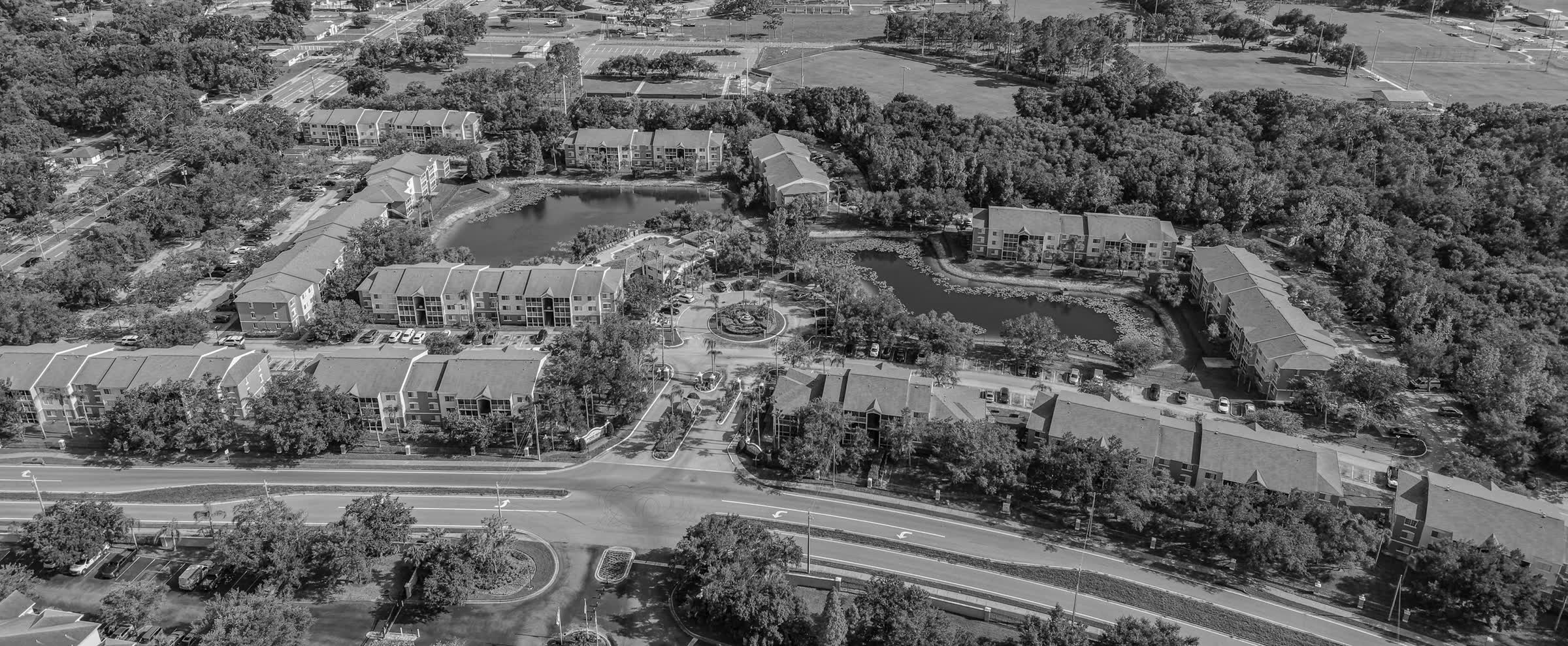Aerial view of a garden-style apartment community with three-story buildings around a lake and pool