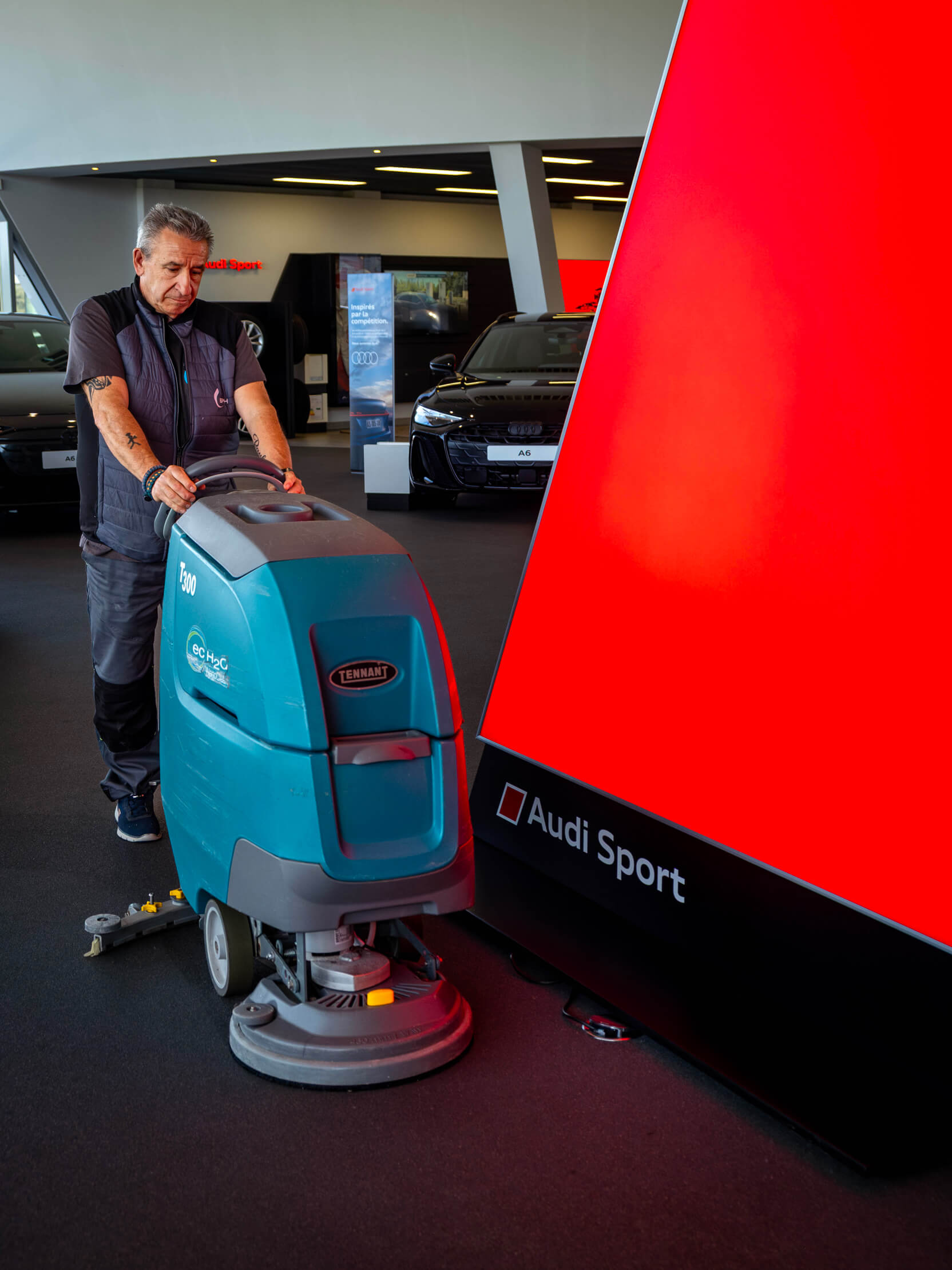 Agent de propreté manœuvrant une autolaveuse dans un hall d'exposition automobile