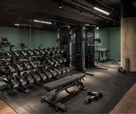 Modern gym area with dumbbell racks, a bench, weight machine, and free weights on a rubber floor.