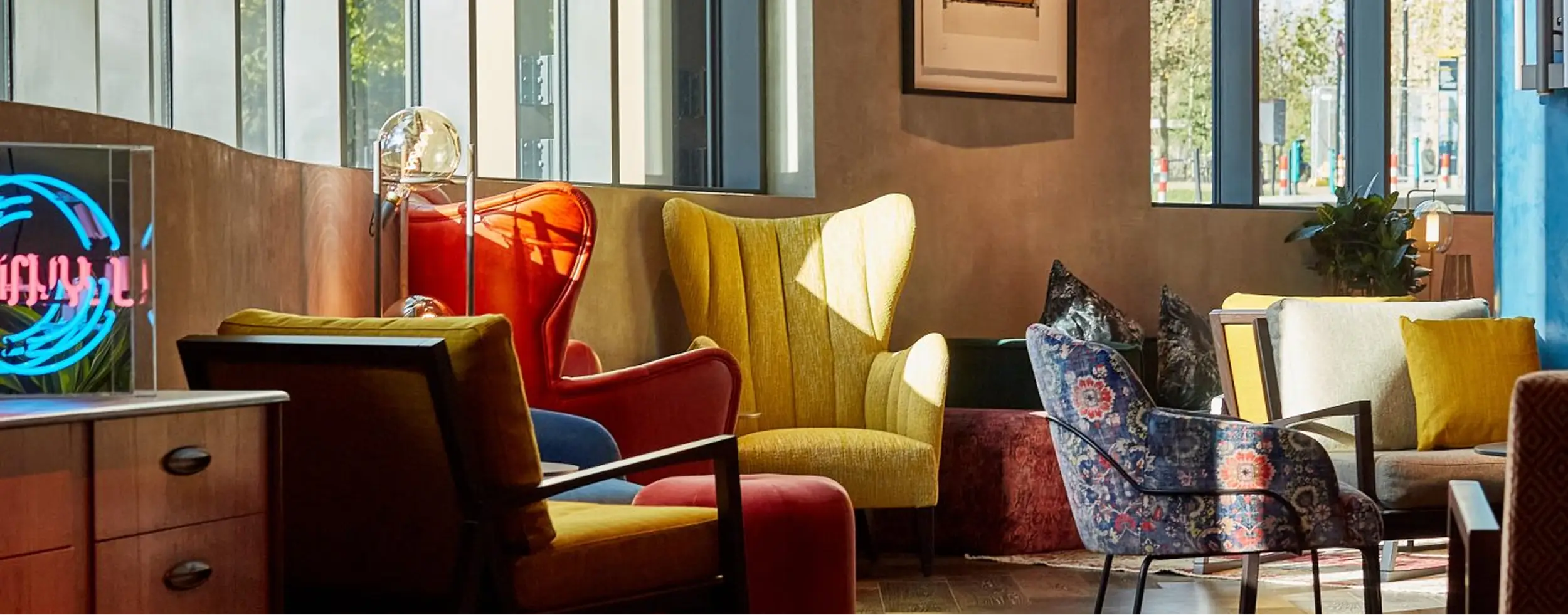 Cozy seating area with colorful armchairs and sofas by large windows in a bright room.
