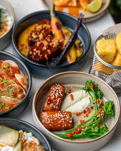 Assorted gourmet dishes including glazed tofu with sesame seeds and broccoli, roasted carrots, and a basket of fried yellow cubes.