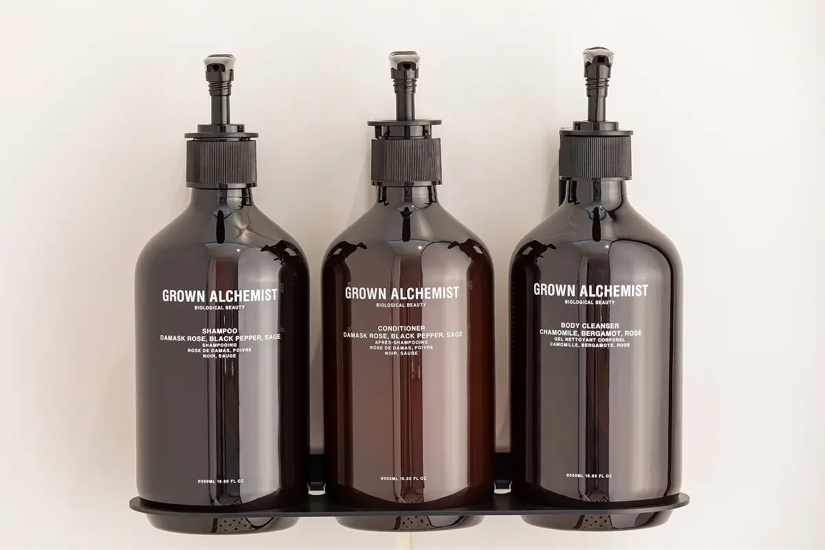 Three amber pump bottles of Grown Alchemist shampoo, conditioner, and body cleanser on a black tray against a white background.