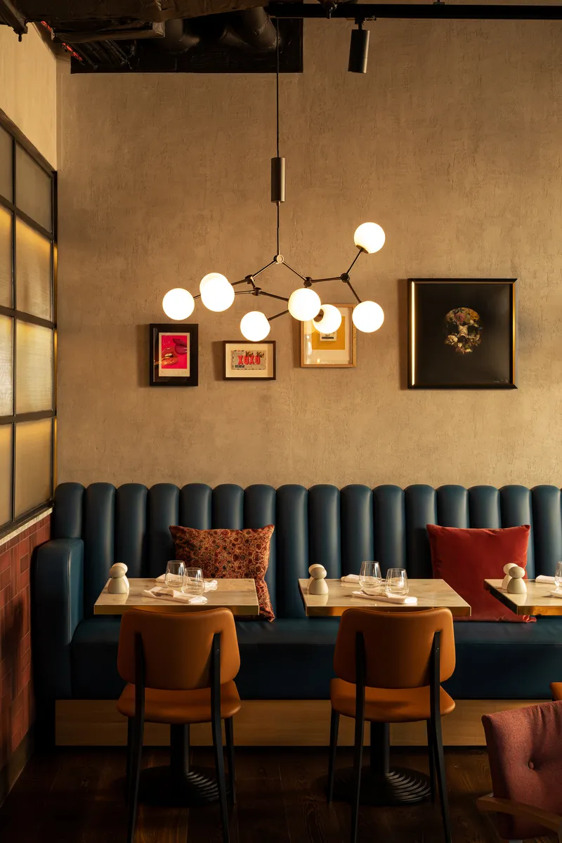 Cozy restaurant seating with blue booth, brown chairs, decorative pillows, and modern chandelier lighting.