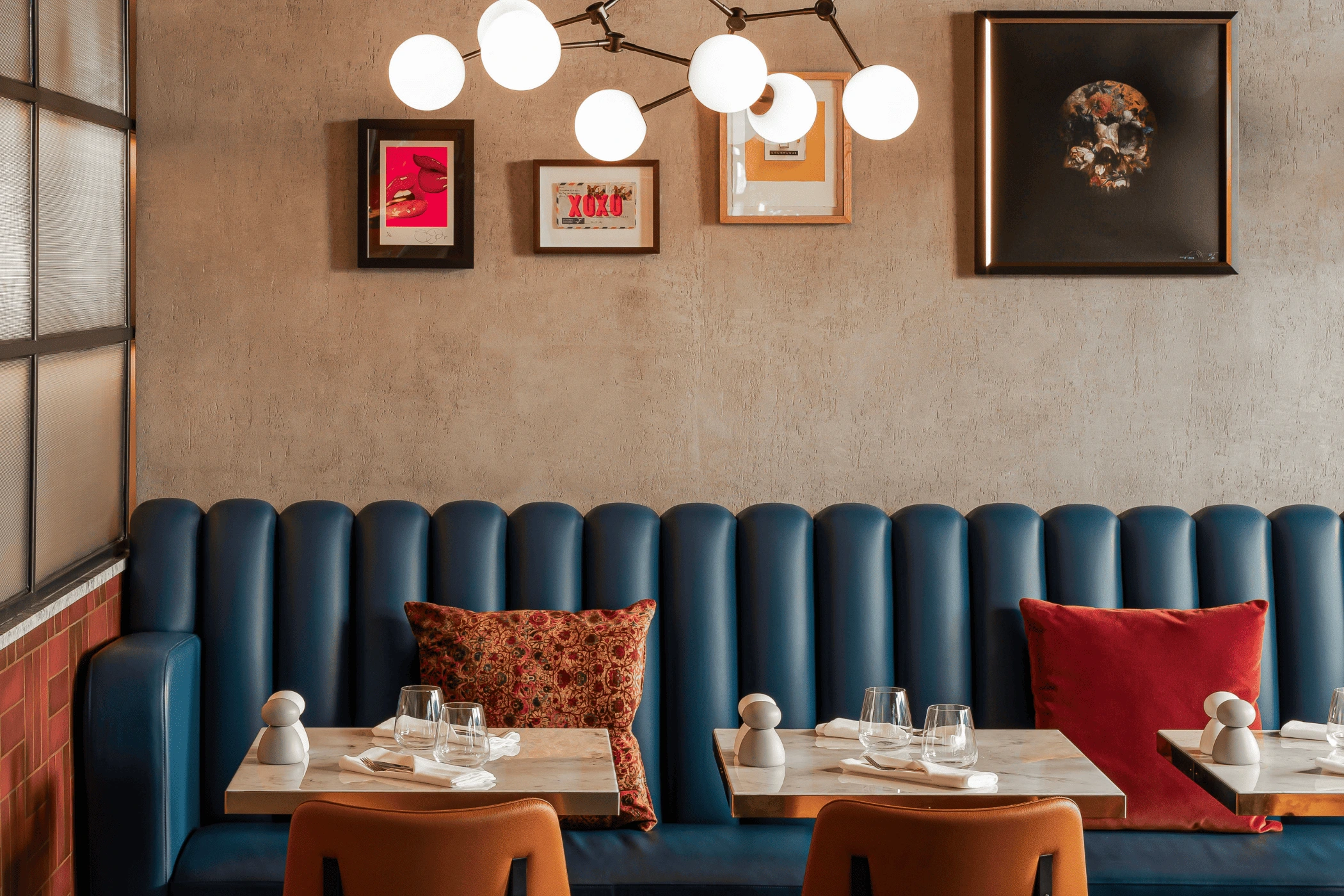 Modern dining area with blue booth seating, marble tables, orange chairs, and framed wall art.