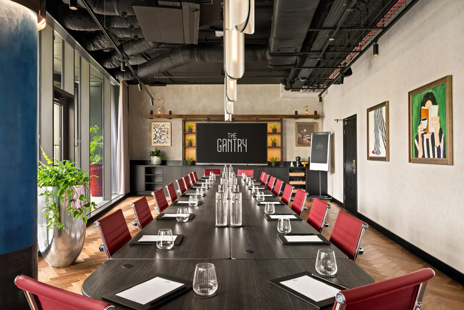 Modern conference room with long table, red chairs, water glasses, notepads, and The Gantry screen.