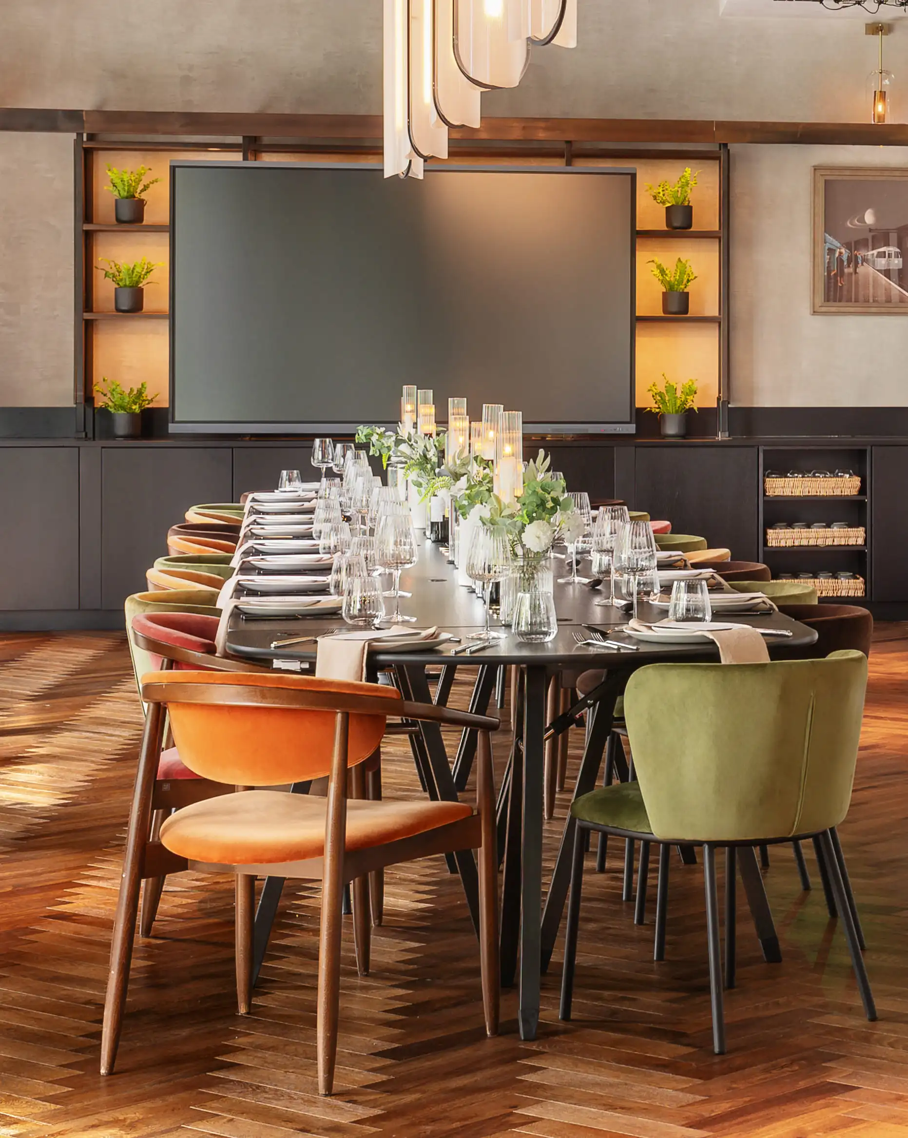 Elegant private dining room with long table, mixed velvet chairs, candles, flowers, and a large screen.
