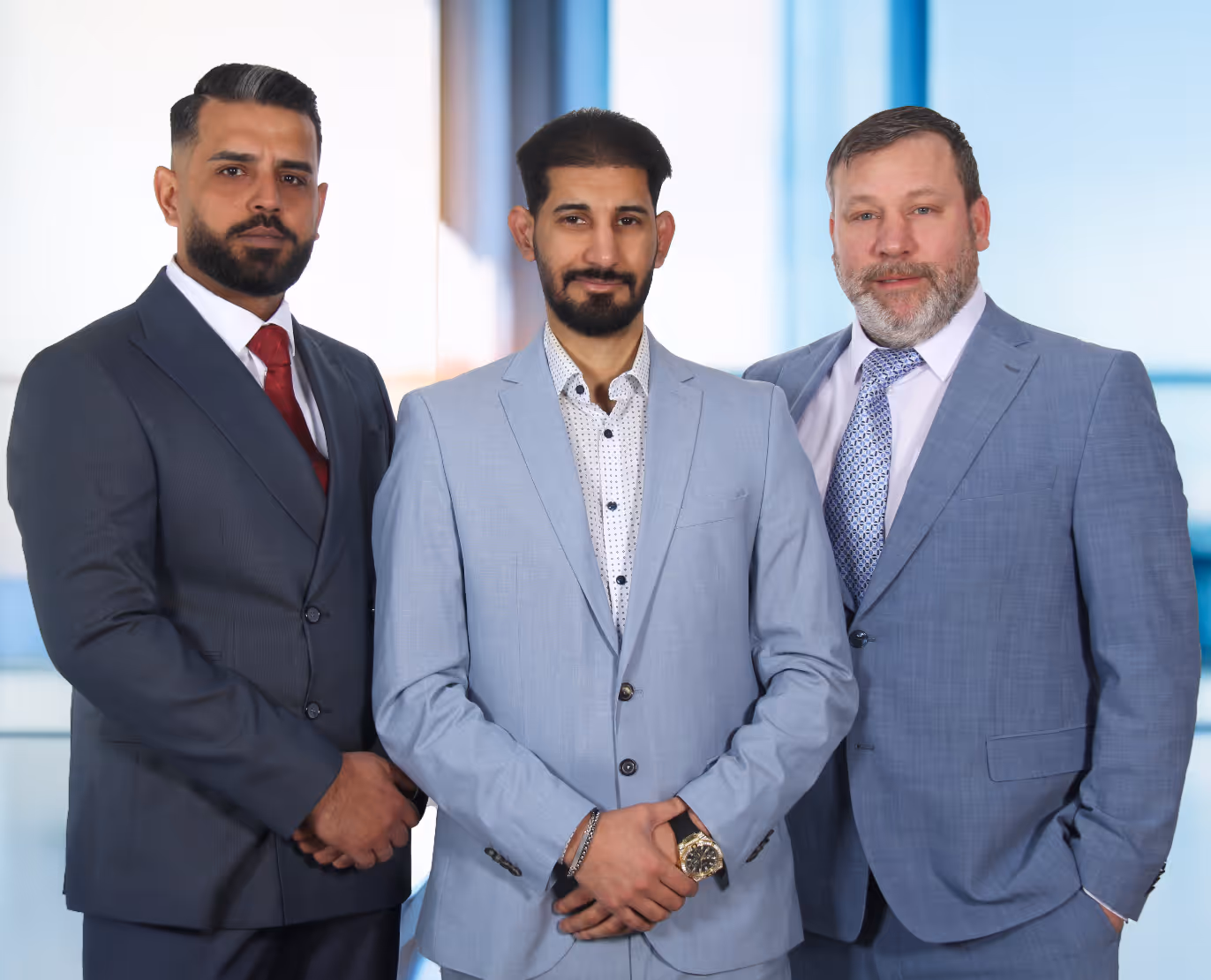 Drei Männer in Business-Anzügen posieren gemeinsam vor einem Bürohintergrund.