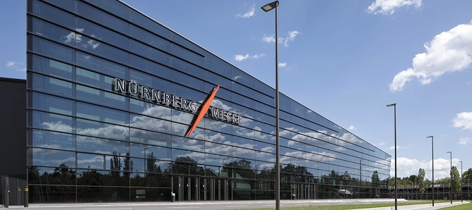 Moderne Glasfassade des Nürnberger Messegeländes mit reflektiertem blauem Himmel und Wolken.