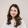 Smiling young woman with long dark hair wearing a white top against a plain light background.