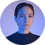 Portrait of a woman with dark hair in a bun, wearing a high-neck black top, illuminated by soft blue and purple lighting