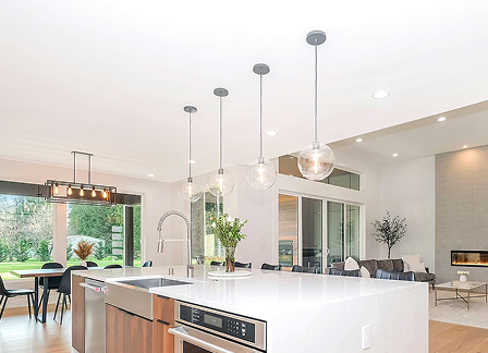 Modern kitchen with white island countertop, hanging glass globe pendant lights, and open dining area with large windows.
