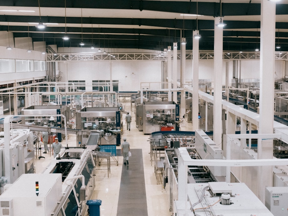 Interior of a large, clean factory with automated machinery and workers wearing gray uniforms and red caps.