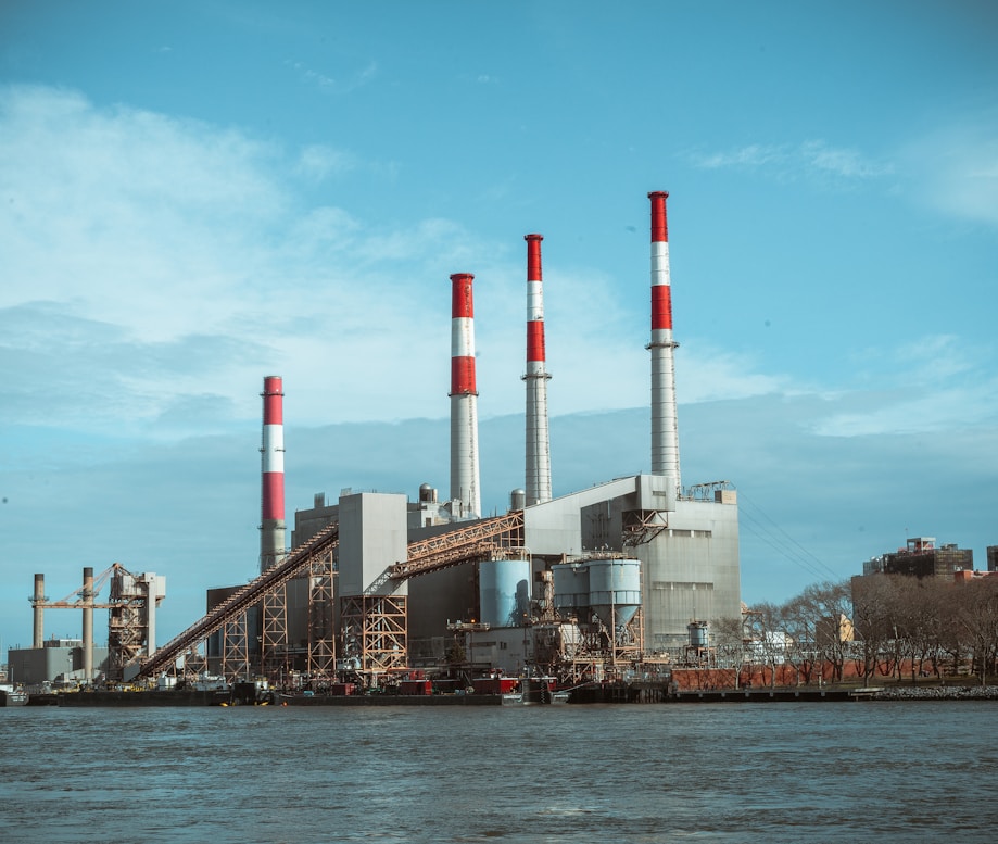 Industrial power plant with four tall smoke stacks with red and white stripes along a waterfront.