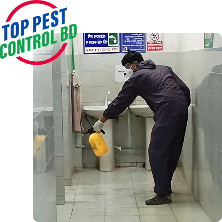 Person in protective clothing and mask spraying disinfectant in a tiled restroom.