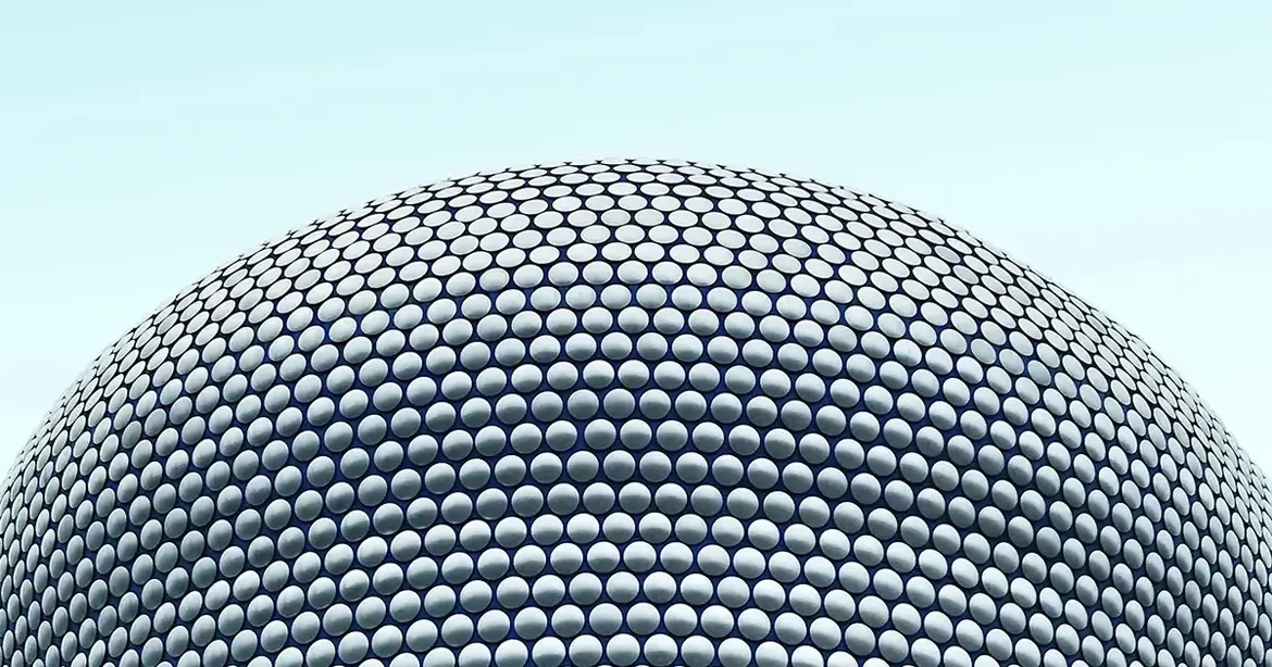 A close-up view of the Bullring Shopping Centre in Birmingham, UK, featuring its distinctive circular pattern of metallic discs against a clear blue sky.