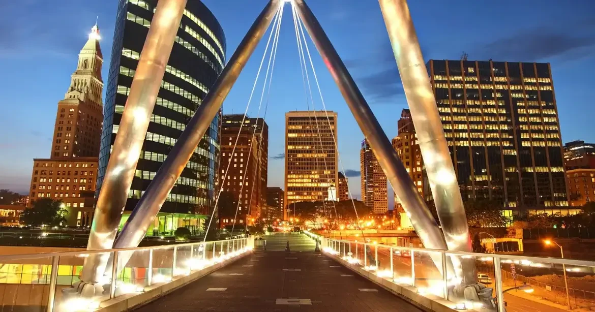A nighttime skyline of Hartford, Connecticut, showing illuminated modern office towers and a distinctive triangular metal-framed building in the foreground