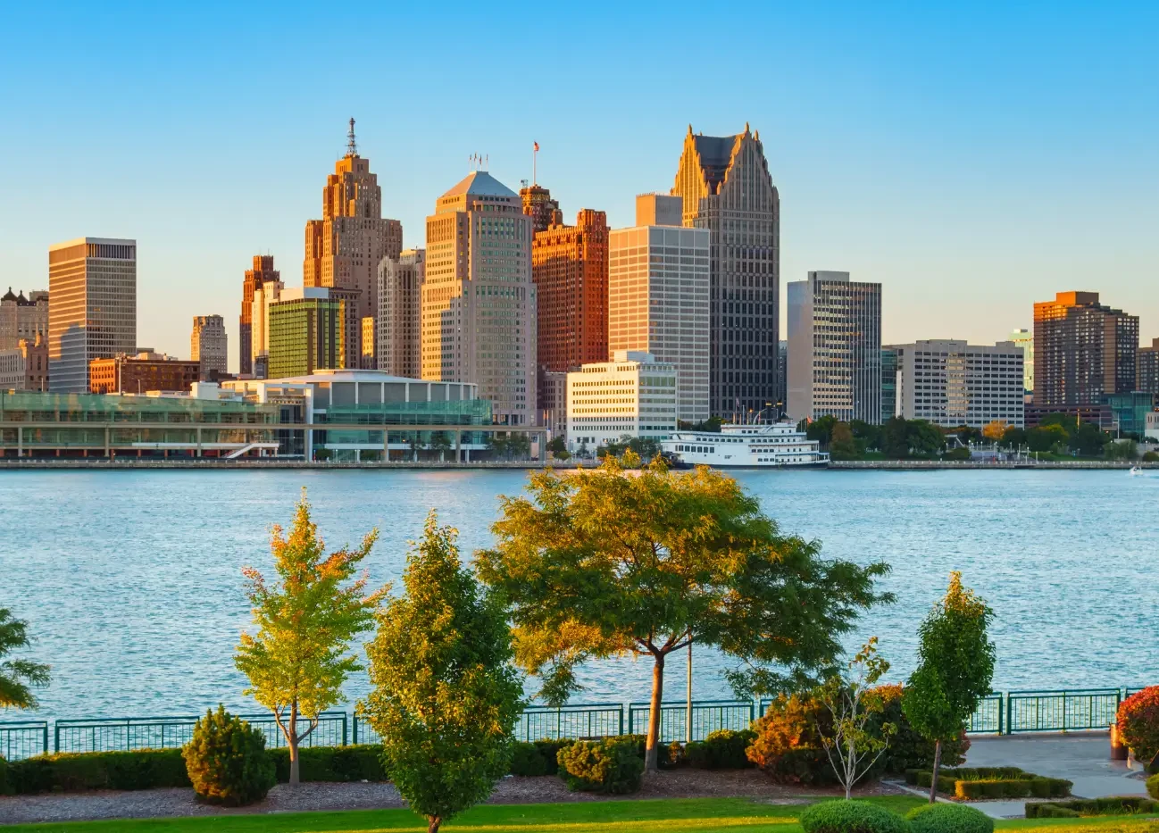 Silhouette of Detroit, Michigan city skyline at sunset with a river in the foreground.