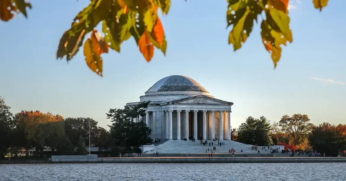 Jefferson Memorial in Washington, D.C., with its iconic dome and columns. The memorial is surrounded by trees with autumn leaves.