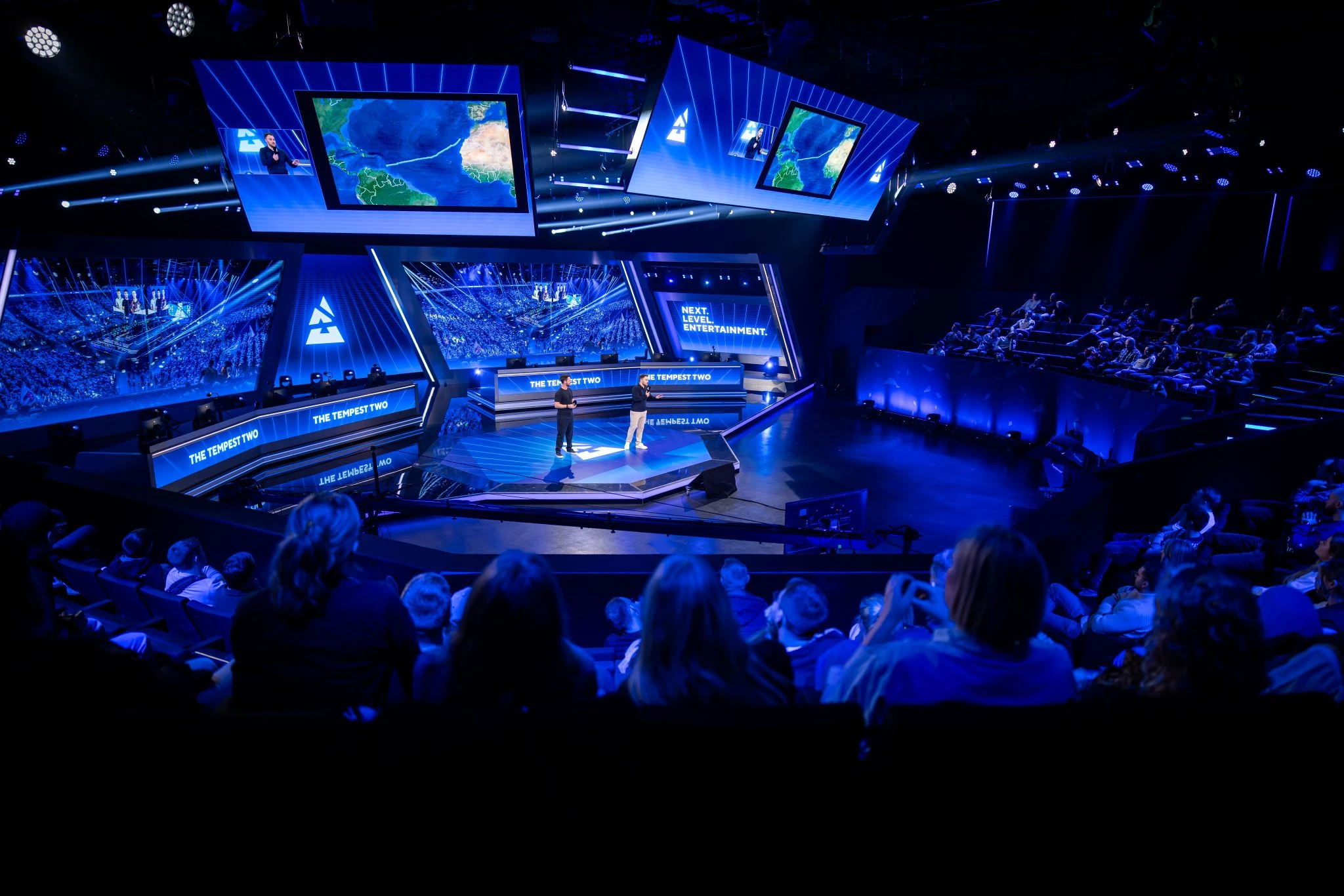 The Tempest Two speaking on stage to a large audience, with the route of their Atlantic row displayed on the screens behind them