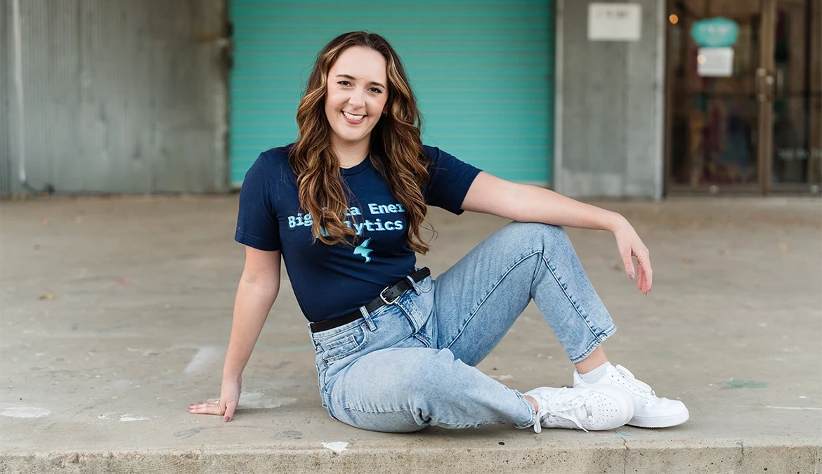 Jess Ramos sitting on a kerb in a navy Big Data Energy Analytics T-shirt