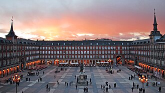 Panoramic view of Madrid Plaza Mayor at sunset with people walking and historic buildings surrounding the square.