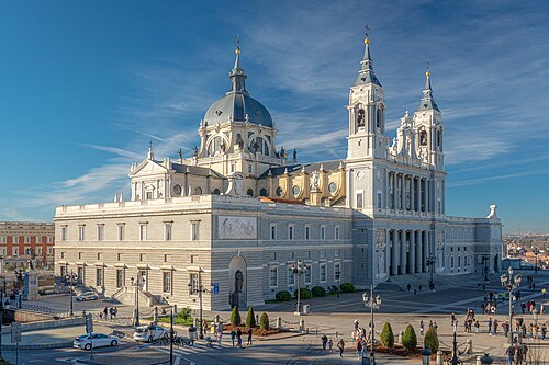 Wide-angle view of the Almudena Cathedral in Madrid with its detailed domes and towers under a blue sky.
