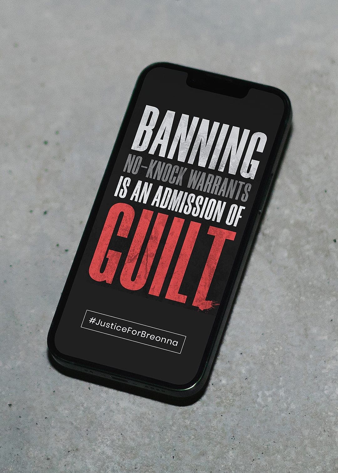 Phone mockup on concrete displaying the text "Banning no-knock warrants is an admission of guilt — #JusticeForBreonna."