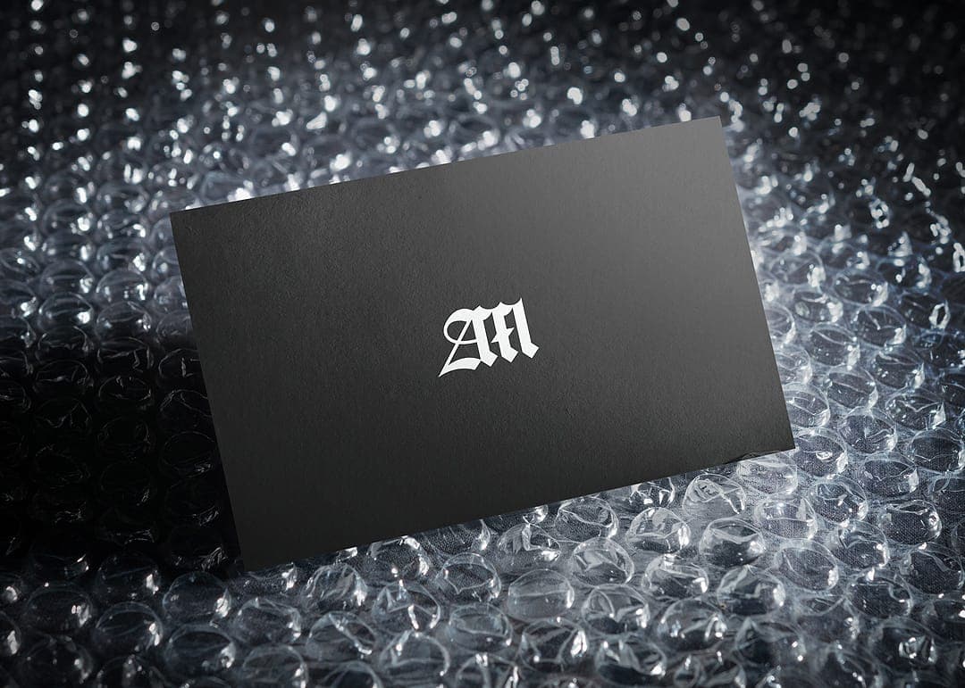 Black business card with a white "AM" monogram, resting on bubble wrap.