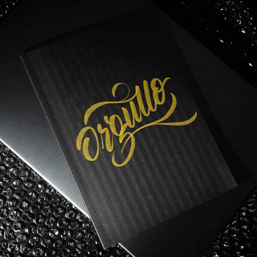 Gold cursive lettering reading "Orgullo" embossed on a black textured book cover.