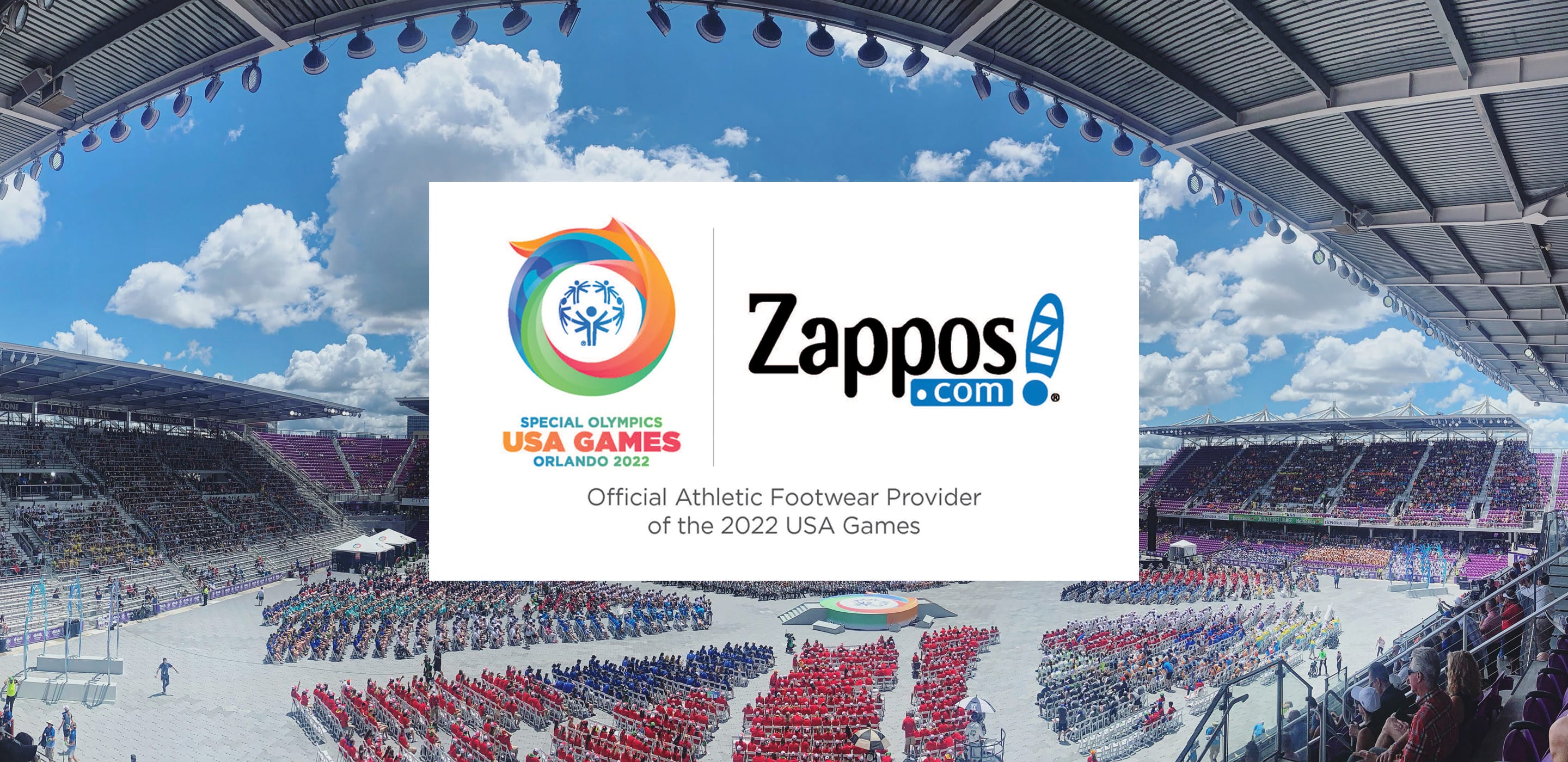 Panoramic view of the 2022 Special Olympics USA Games Orlando opening ceremony, with athletes seated in color-coded sections on the field, overlaid with a graphic reading "Special Olympics USA Games Orlando 2022 · Zappos.com — Official Athletic Footwear Provider of the 2022 USA Games.