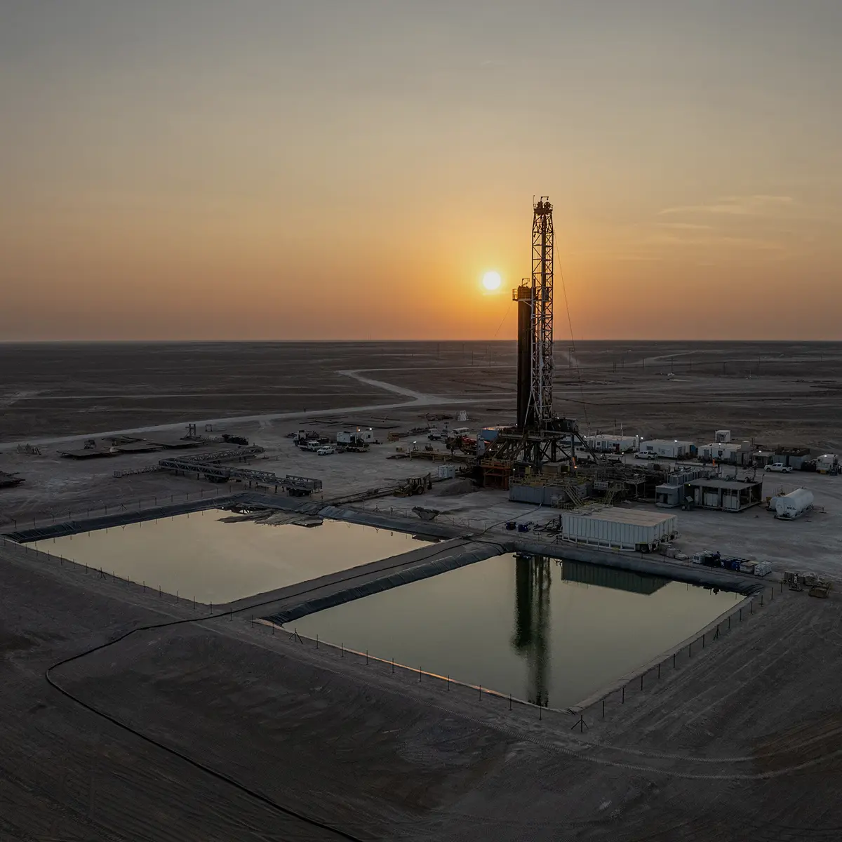 Drilling rig and reserve pits at sunset in the desert