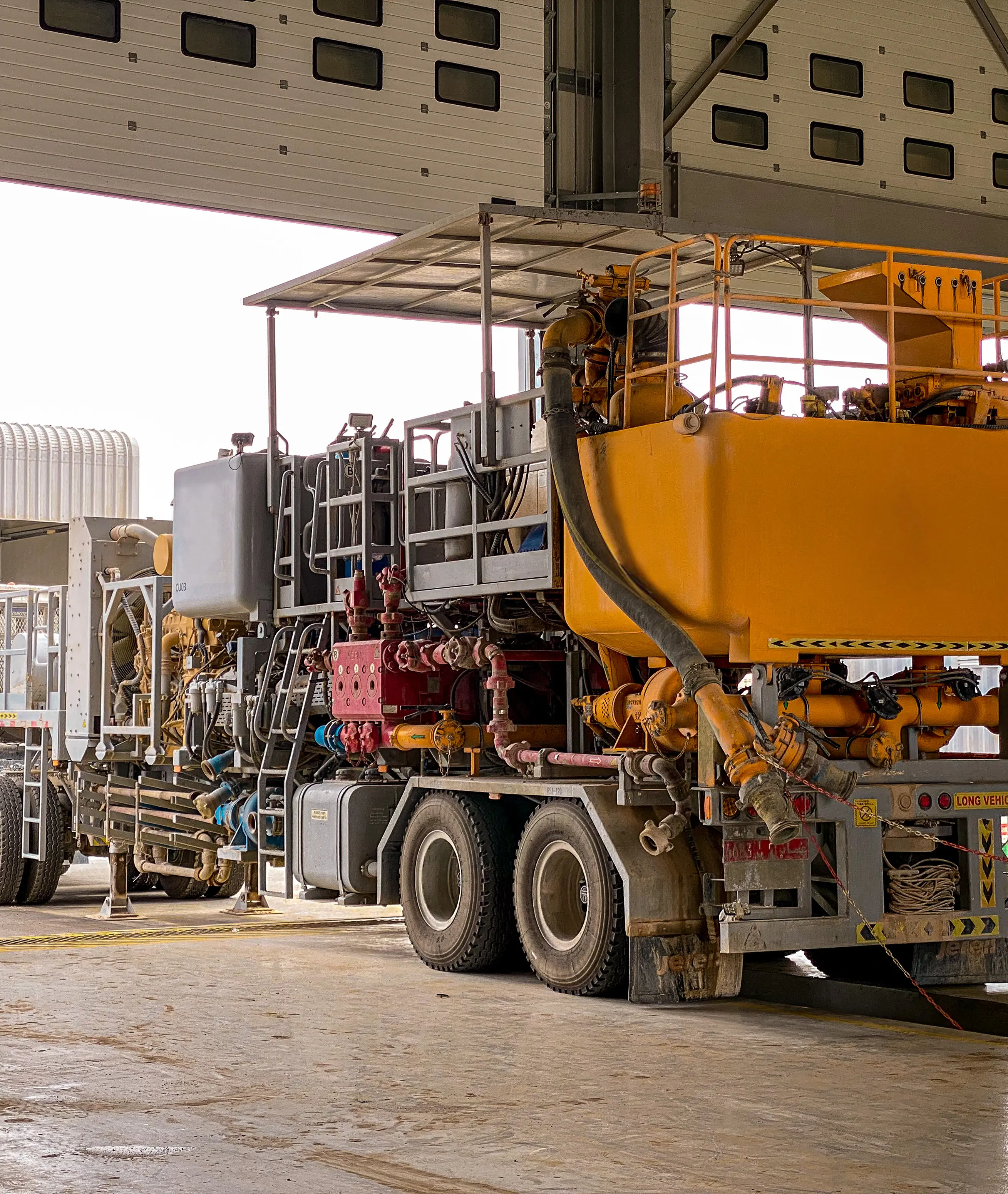 Orange cementing unit parked under a workshop canopy