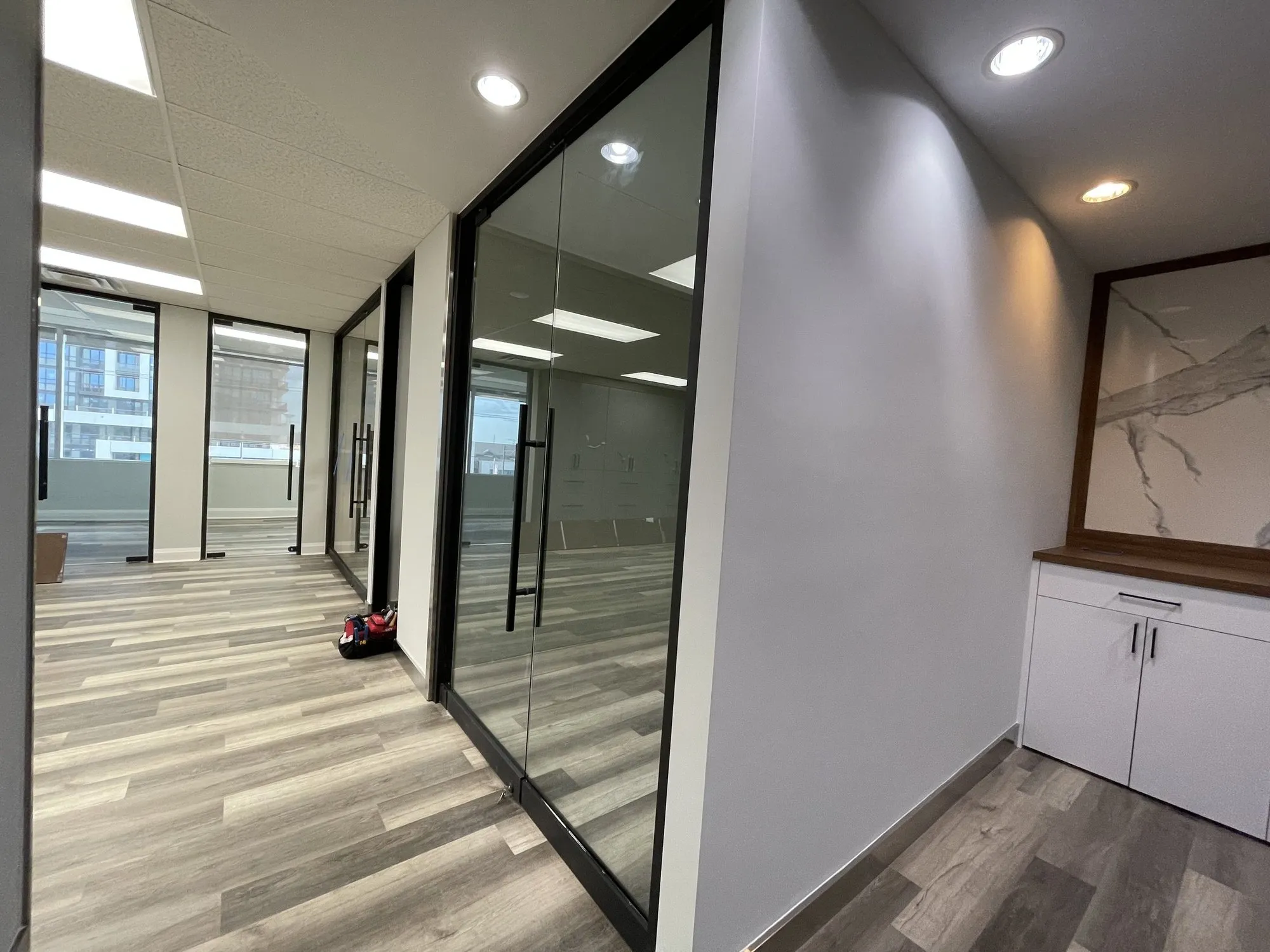 Corridor of full-height black-framed glass private offices in a completed Richmond Hill office fit-out by Buildup Contracting