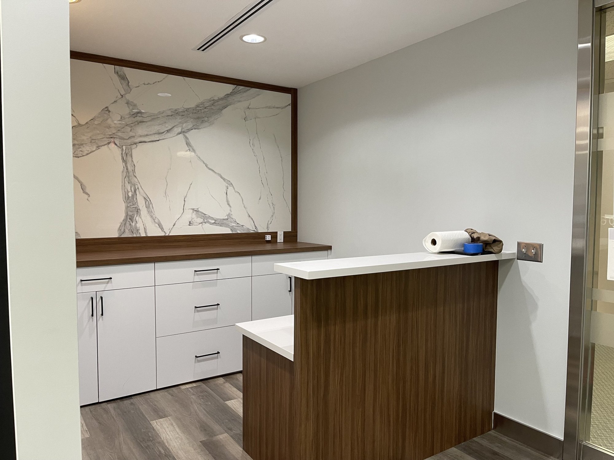 Reception of a completed 2,000 sf insurance office fit-out in Richmond Hill — marble-look porcelain feature panel in a walnut surround with custom white cabinetry