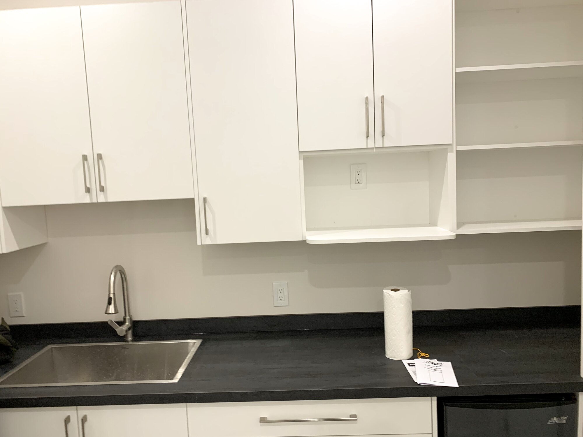 Office kitchenette with white cabinetry, open shelving and a dark countertop built during a Richmond Hill office fit-out