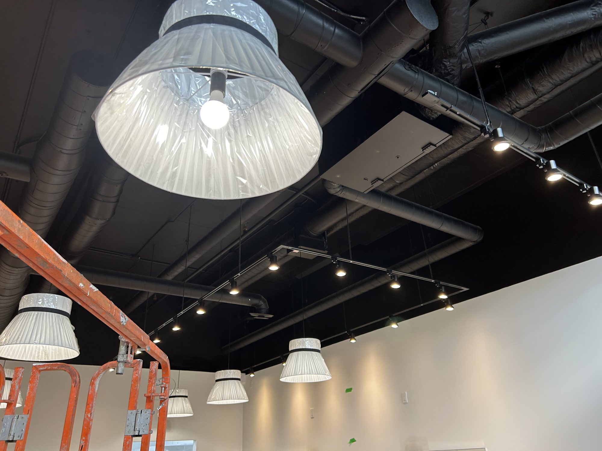 Track lighting and pendant fixtures installed on the black open ceiling of a bubble tea shop