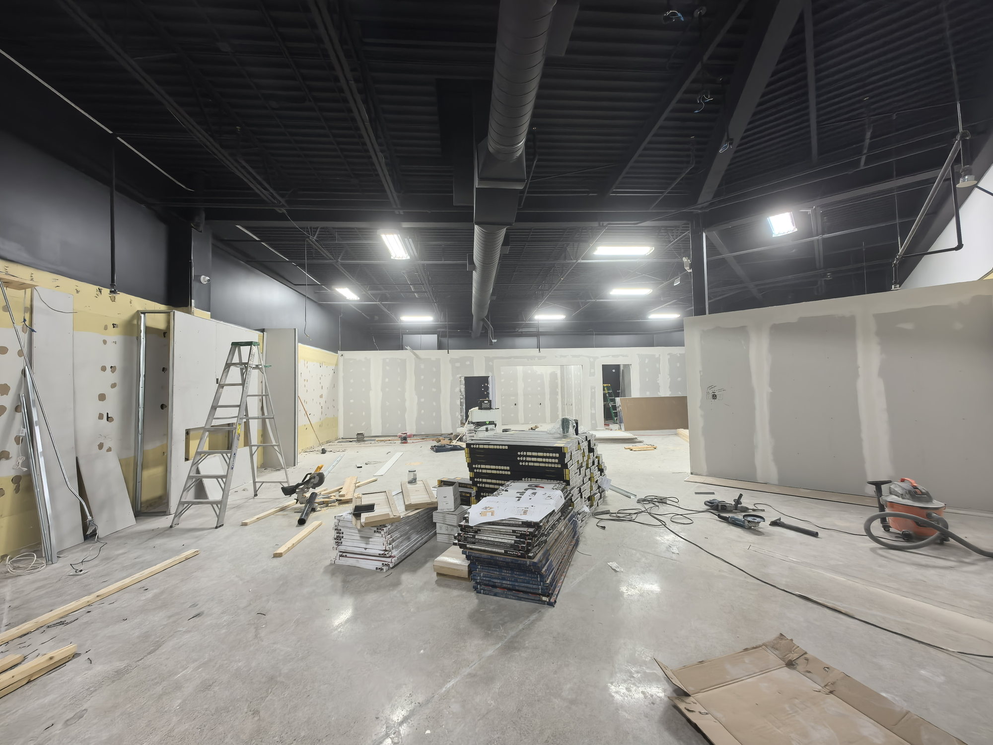 Exposed roof structure and ductwork painted black above white drywall partitions in a showroom build