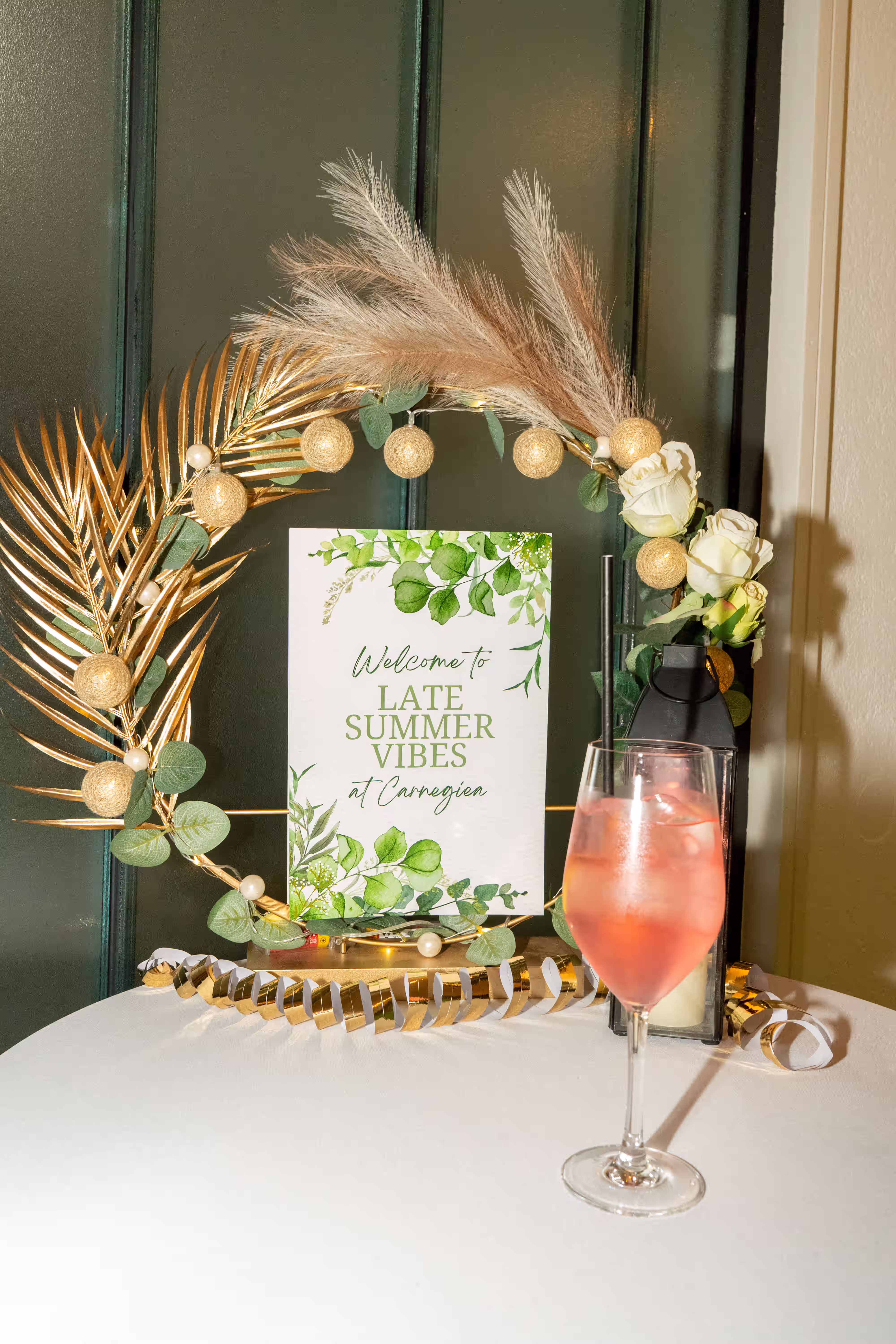 Begrüßungsschild 'Late Summer Vibes' mit goldener Deko, weißen Rosen und einem rosa Getränk im Glas.