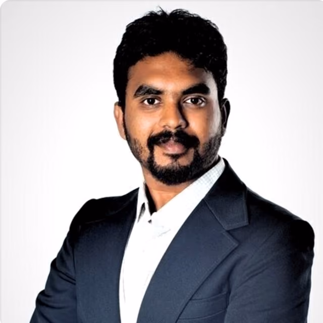 Man with a beard and mustache wearing a dark suit jacket and white shirt against a white background.